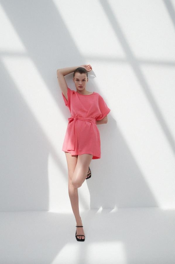 Diseño fluido con cuello redondo y manga corta acabada en vuelta para este mono corto de Zara en color rosa con cinturón a tono que cuesta 25,95 euros y está disponible entre las tallas XS y XXL.