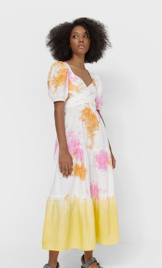 En tonos anaranjados y rosados sobre fondo blanco y volante en amarillo pastel en el bajo, este vestido largo de popelín viene con escote de pico, manga corta abullonada y detalle de lazo a tono que entalla la cintura. Cuesta 29,99 euros y está disponible entre las tallas XS y XL.