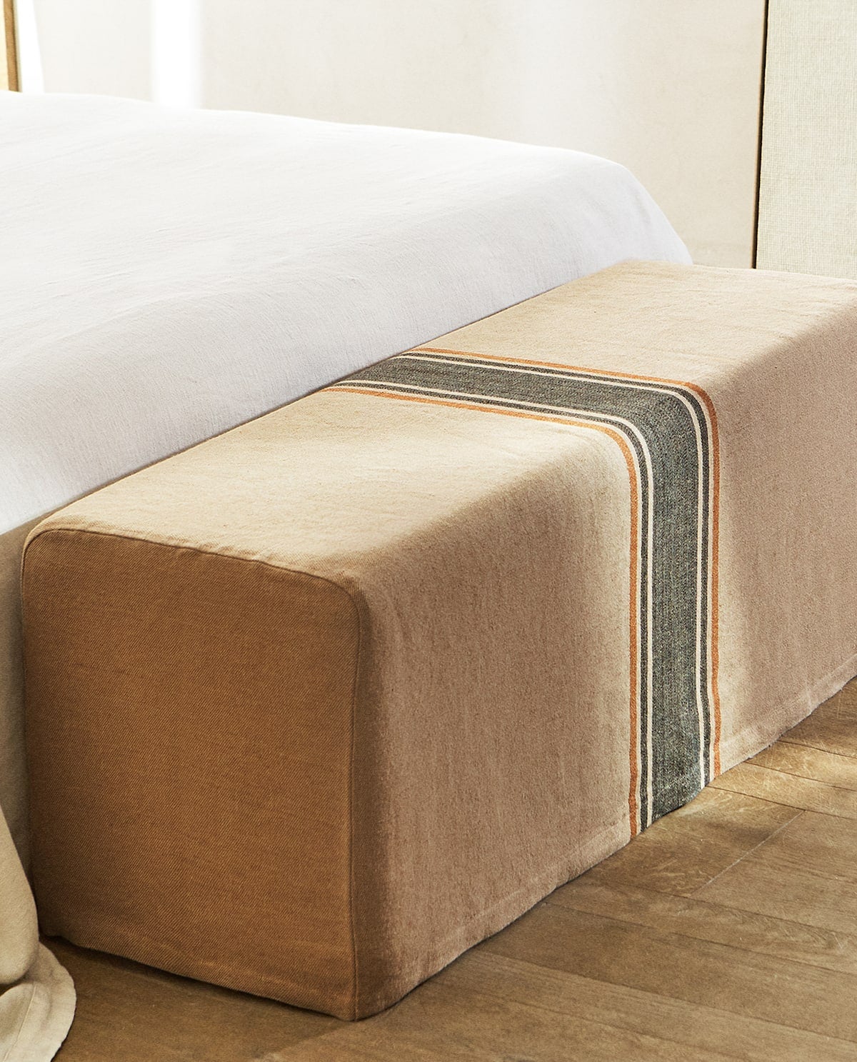 Banco de madera con estructura acolchada y funda de yute, lino y algodón en color natural con raya estampada a contraste. Ideal para decorar los pies de la cama. (199 euros).