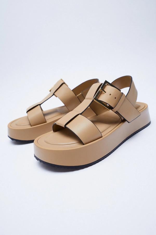 En color beige, esta sandalia de piel con plataforma y tiras de piel cuenta con una tira envolvente elástica alrededor de tobillo y cierre mediante hebilla. Tiene un precio de 49,95 euros.