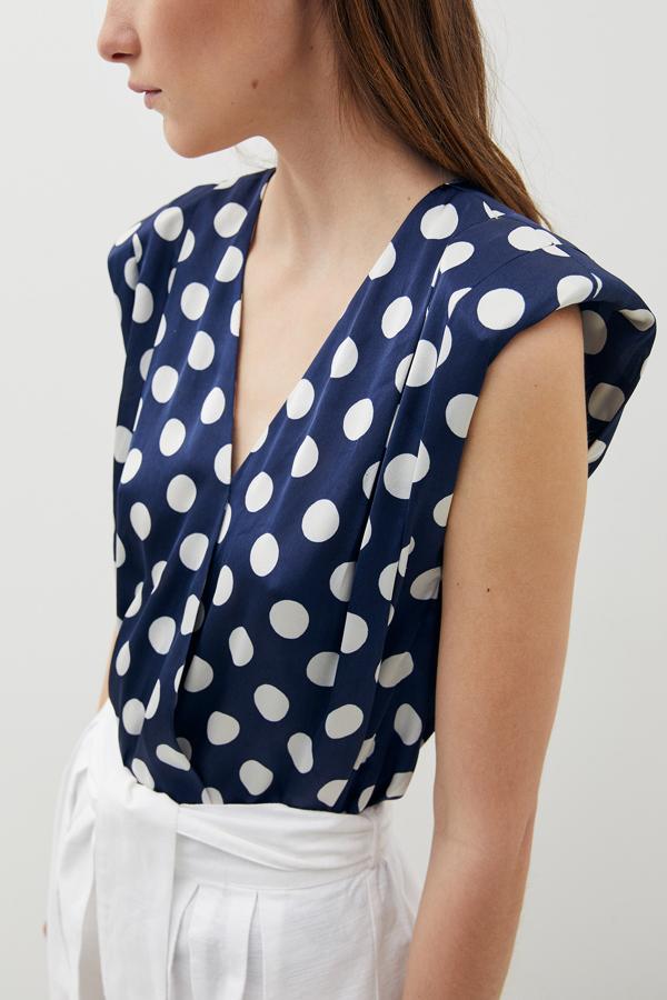 Con cuello de pico y hombreras, esta bonita blusa en azul marino con estampado de lunares blancos en tejido satinado cuesta 13,99 euros y está disponible en las tallas S, M y L.