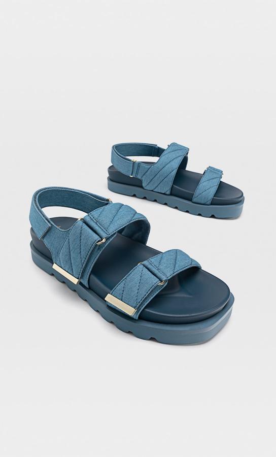 El color azul denim, esta sandalia plana con tiras acolchadas y suela dentada cuenta con cierre mediante tira adherente y tiene un precio de 25,99 euros. Es de Stradivarius.
