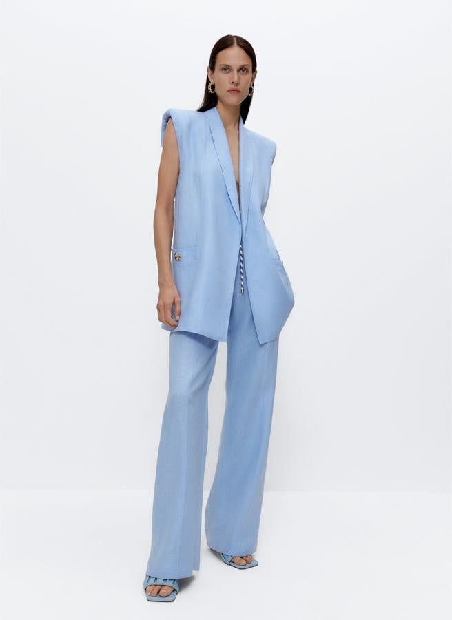 En color azul celeste, este chaleco largo de lino con bolsillos delanteros con botón dorado y hombreras tiene un precio de 129 euros.