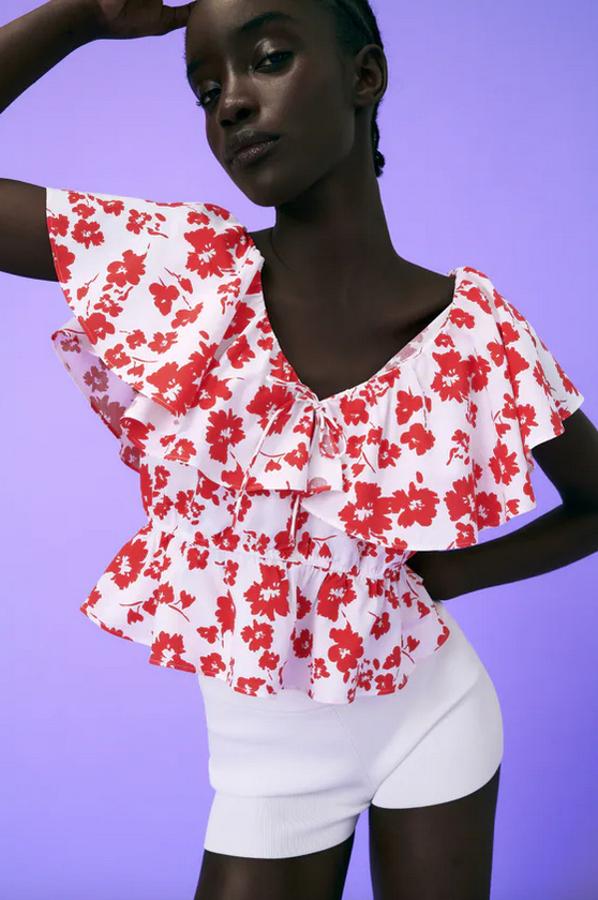 Escote de pico con lazo y mangas cortas con volante para esta blusa blanca con estampado de flores rojas que costaba 25,95 euros y ahora podemos encontrar por 17,99 euros.