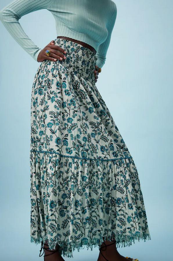 Cintura elástica tipo nido de abeja para esta falda blanca de tiro alto con estampado de flores en tonos azules y bajo asimétrico que costaba 39,95 euros y ahora podemos comprar por 19,99 euros.