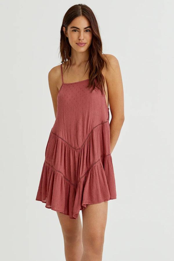 Este vestido corto de plumeti en color rojizo cuenta con tirantes finos, escote recto y detalle de calados y volantes. Tiene un precio de 22,99 euros.