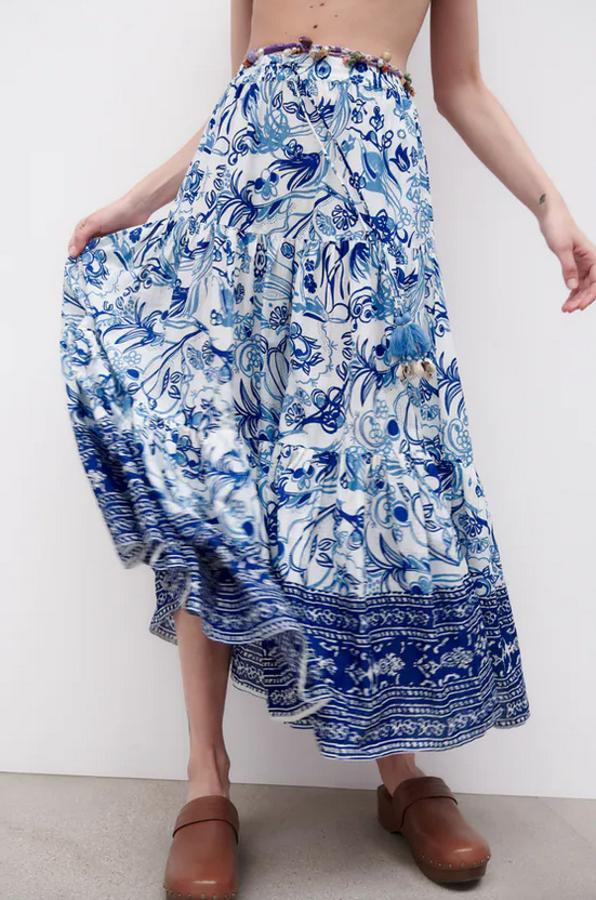 De tiro alto y cintura elástica ajustable con cordones, esta falda de fondo blanco con estampado de flores en color azul viene con bolsillos laterales ocultos en costura y detalle de conchas y borlas combinadas a tono. Podemos encontrarla entre las tallas XS y XXL por 29,95 euros. 