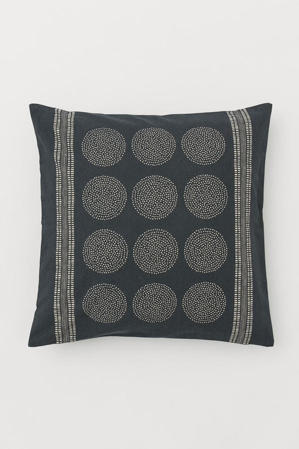Disponible en gris o en beige, esta funda de cojín en lona de algodón orgánico con estampado tiene una medida de 50x50 centímetros y un precio de 2,99 euros. Es de H&M.