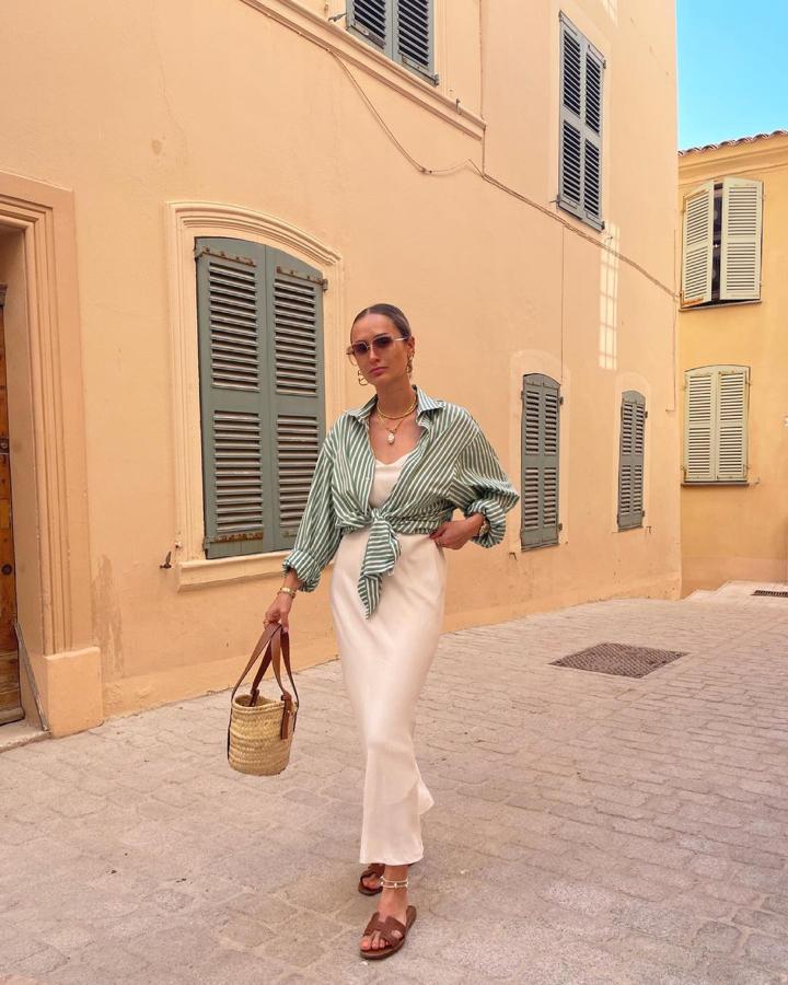 Un vestido lencero, ya de por sí, queda genial. Pero, si le metemos una camisa anudada, le damos una nueva dimensión al look, más juvenil y no tan simple. Sandalias destalonadas marrones son básicas en el calzado veraniego. Un bolsito mono. Y, ¡Lista!