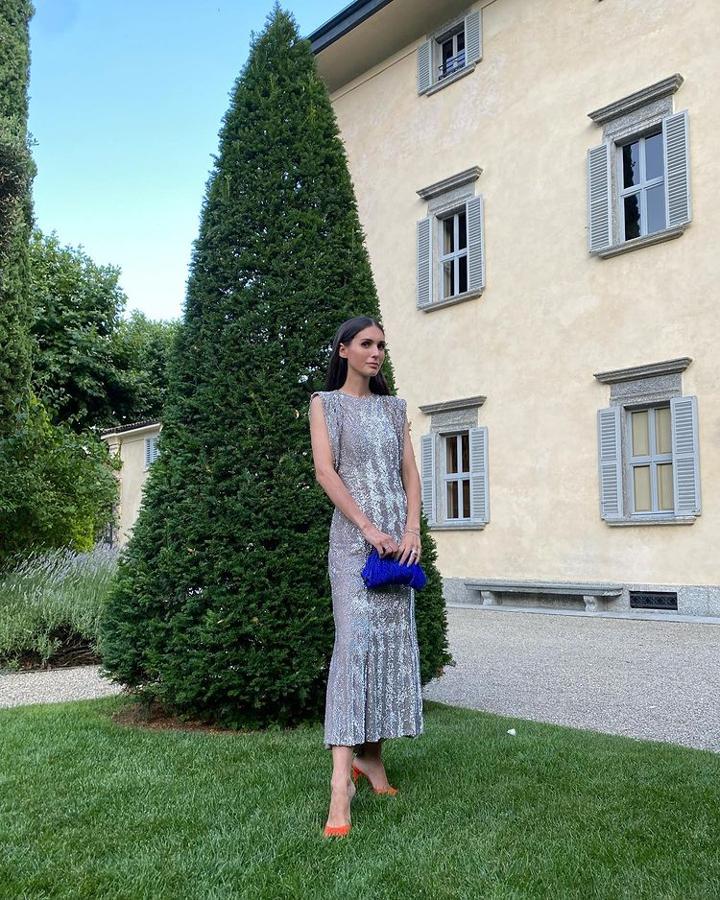 La 'it girl' luce un vestido plateado de tejido brillante, con hombreras y mangas con caída. Termina el look con 'mules' de tacón naranjas y 'clutch' azul.