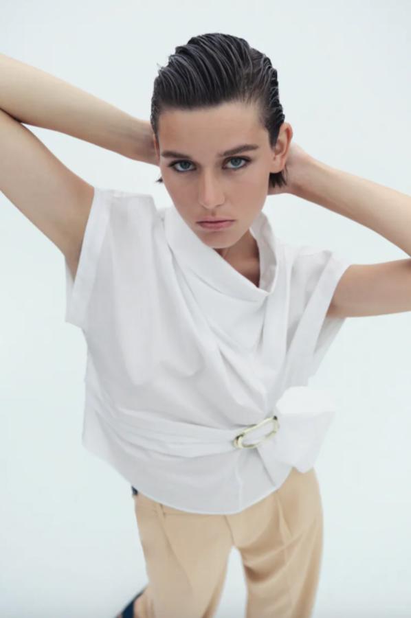 De cuello subido y manga corta, este top confeccionado en popelín en color blanco viene con detalle de hebilla metálica en la cintura y cuesta 25,95 euros. Está disponible entre las tallas XS y XL. 