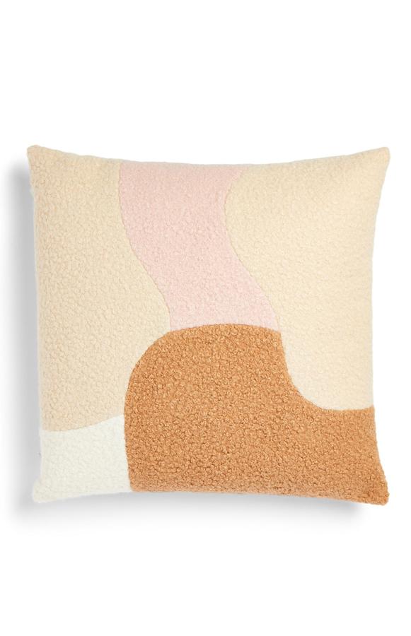 Con panel de tejido rizado en tonos naturales, este cojín tiene un precio de 10 euros.