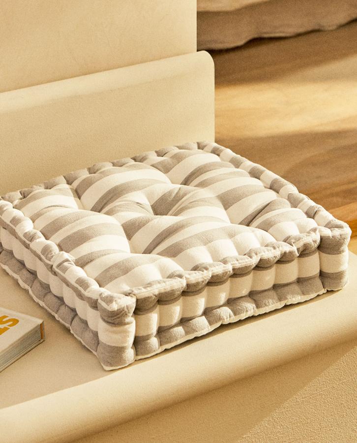 Disponible en gris o en amarillo, este cojín de suelo de algodón con estampado de rayas tiene una medida de 45x45 centímetros y un precio de 19,99 euros.