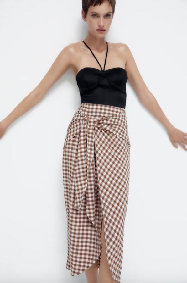 Marrón y color crudo en estampado vichy para esta falda tipo pareo de Zara con lazada lateral y cierre de botón interior. Disponible entre las tallas XS y XL, cuesta 25,95 euros. 