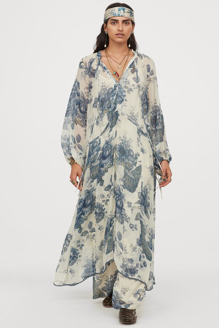 Diseño holgado para este vestido largo en crepé de gasa fluida con estampado floral en tonos azules. Tiene escote de pico con tiras de anudar y cordón de ajuste en el escote y la cintura. Con mangas raglán largas con ajuste en los puños y bajo asimétrico con ribete de pompones tiene un precio de 59,99 euros. 