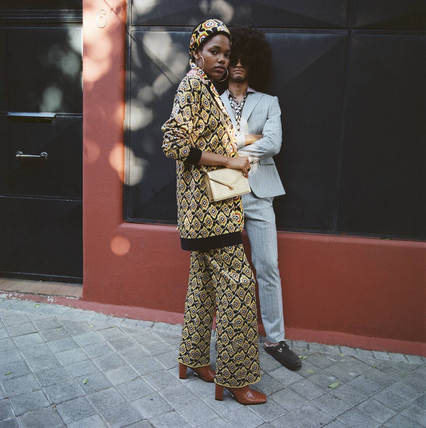 ella va con pañuelo en la cabeza, chaqueta y pantalón, todo de Maliparmi; botas de Guess; aros dorados de Zara; bolso de Bvlgari y anillo de Thomas Sabo. Él lleva traje, camisa y corbata, todo de Hugo Boss; y zuecos de Birkenstock