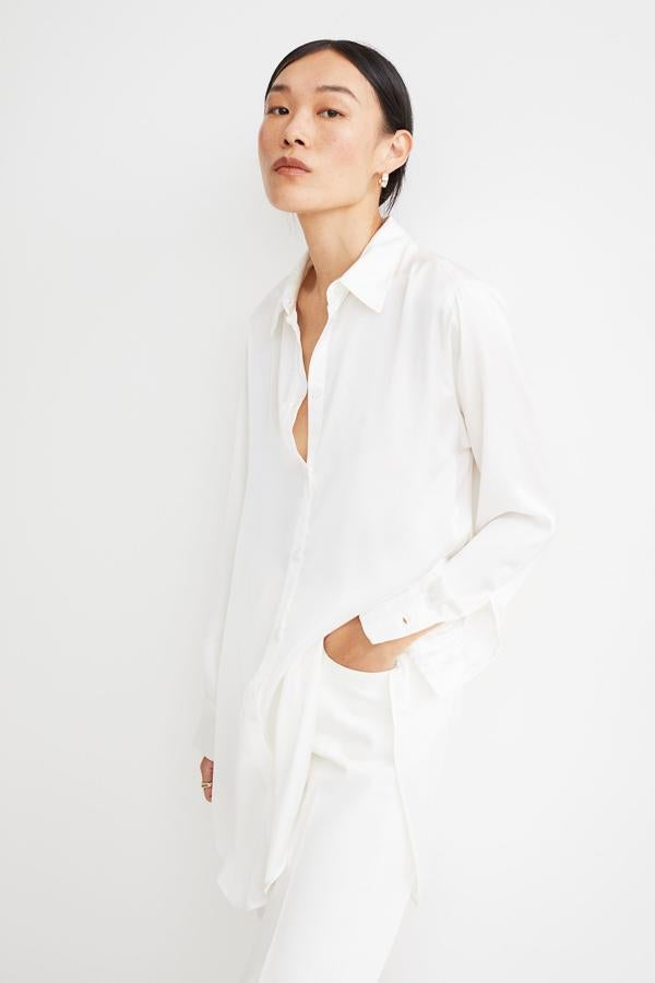 Con diseño clásico y botones en la parte delantera, esta camisa de satén en color blanco cuenta con suave caída y bajo redondeado. Es de H&M y tiene un precio de 19,99 euros.