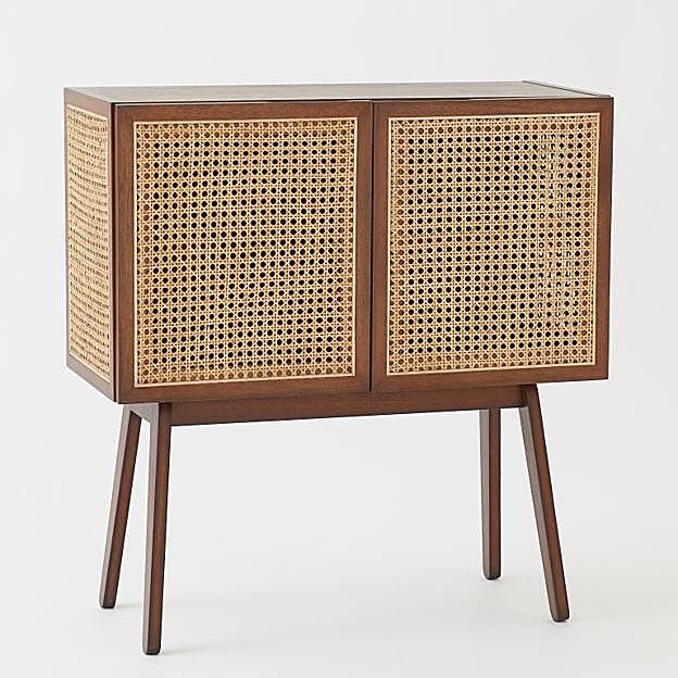 Imagen principal - El mueble de dos puertas en ratán cuesta 299 euros en H&M Home, el sillón cuesta 249 euros, y las lámparas, 119 euros.