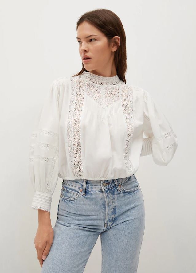 Otra opción romántica para llevar con vaqueros, esta blusa blanca con detalles bordados y jaretas está rebajada en Mango a 29.99 euros.