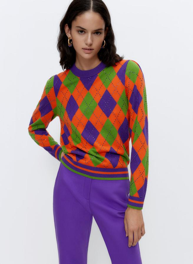 En tonos naranjas, verdes y morados, este jersey de punto de Uterqüe con estampado de rombos y detalle de apliques de brillos viene con cuello redondo y mangas largas. Con acabados en rib en los puños y el bajo, podemos encontrarlo en las tallas S, M y L y cuesta 99 euros.