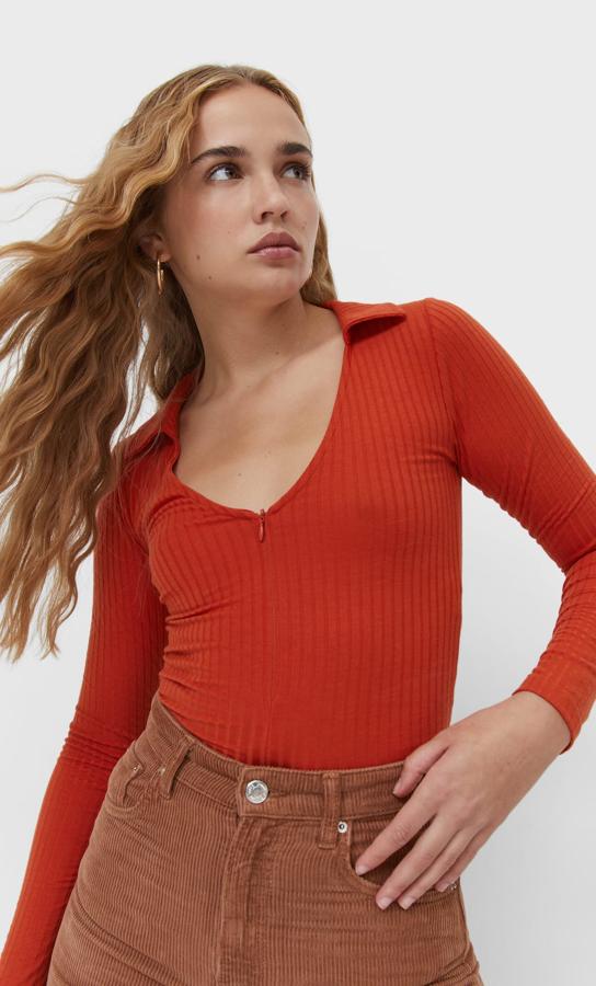 Con escote de pico con cremallera, cuello de solapa y mangas largas, este polo de Stradivarius en naranja tiene un precio de 12,99 euros y podemos encontrarlo entre las tallas XS y XL. 