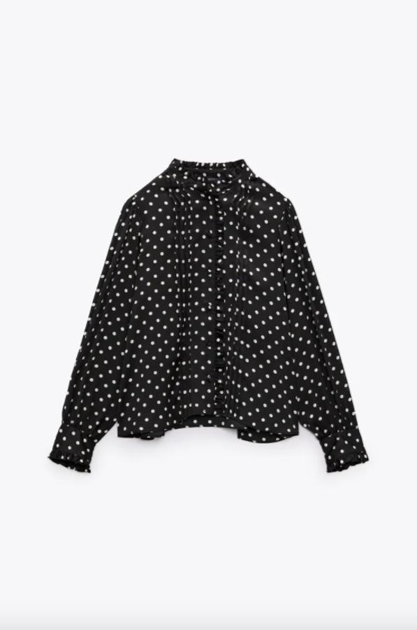 En color negro con estampado de lunares en blanco, esta camisa de cuello subido con volante y detalle de jaretas delanteras, tiene mangas largas y cierre frontal de botones forrados a tono. Disponible entre las tallas XS y XL, tiene un precio de 25,95 euros. 