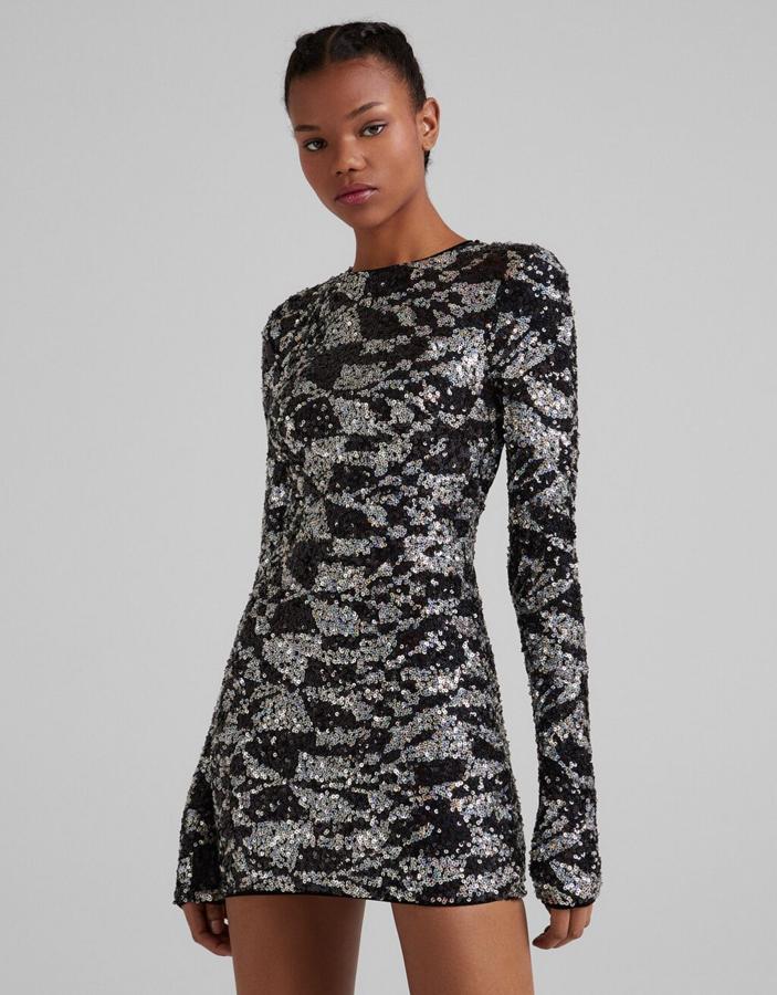 Este vestido mini de lentejuelas en plateado y negro con mangas largas, cuello redondo y estampado psicodélico es de Bershka, cuesta 39,99 euros y está disponible entre las tallas XS y XL. 