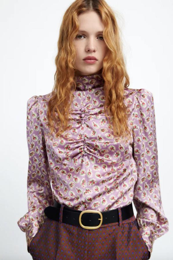 No es estrictamente una camisa, sino un cuerpo, pero es tan bonito que no nos hemos resistido a traerlo aquí. En lila, con estampado de flores en rojo y verde, confeccionada en tejido satinado y con cuello subido y hombros marcados, viene con detalle de frunces delanteros con botones forrados a tono y cierre en espalda. Tiene un precio de 25,95 euros. 