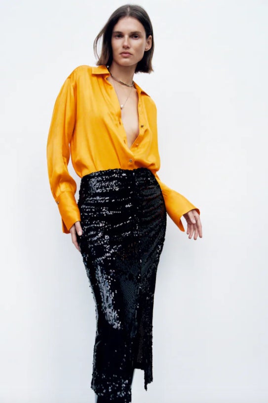 En color mandarina, con cuello de solapa, escote de pico y mangas largas acabadas en abertura, esta camisa satinada de Zara que viene con cierre frontal de botones dorados tiene un precio de 39,95 euros y está disponible entre las tallas XS y XL.