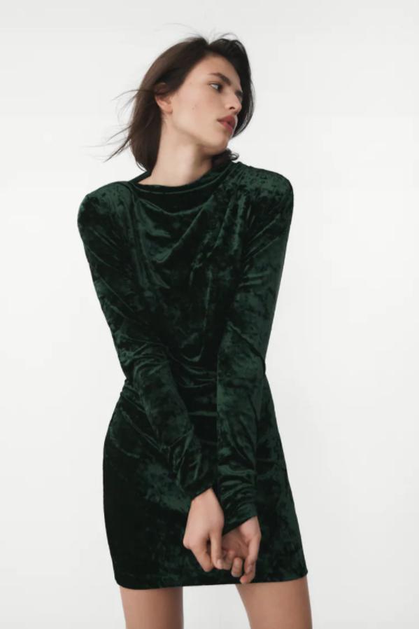 En verde botella y con cuello fluido, este vestido drapeado en terciopelo, con mangas largas con hombreras es de Zara, cuesta 39,95 euros y está disponible entre las tallas XS y XL. 