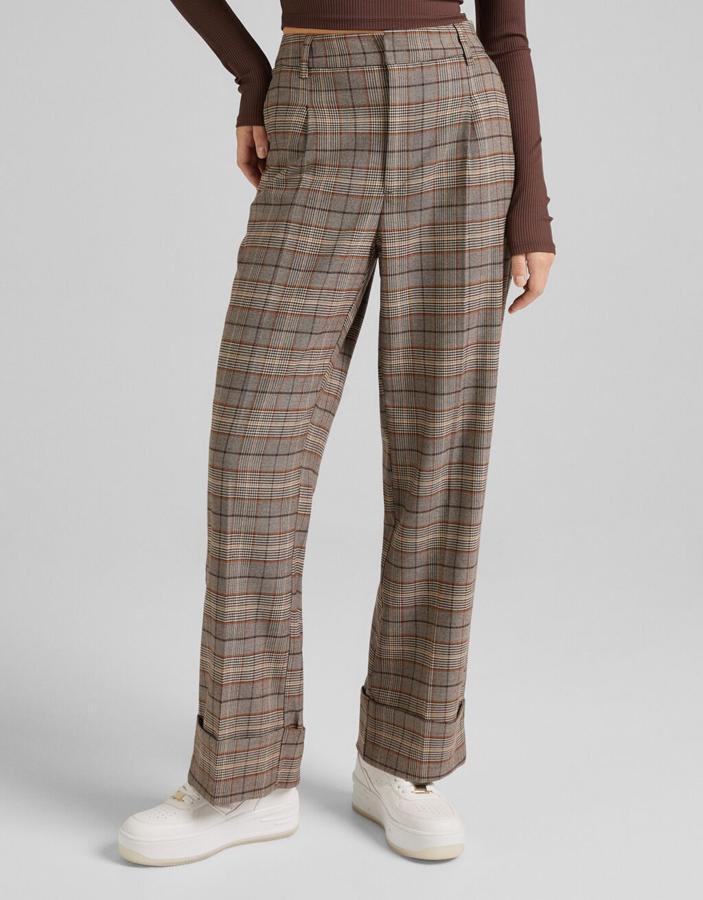 En tonos marrones y con estampado de cuadros Príncipe de Gales, estos pantalones de Bershka con pernera amplia, bajos subidos y pinzas frontales cuesta 25,99 euros y está disponible entre las tallas 32 y 44.