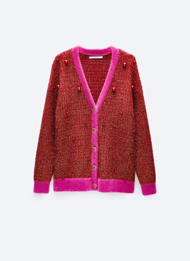 Confeccionado en punto brillo en rojo, con apliques de perlas fantasía a tono y puños, bajo y cierre a contraste en fucsia, este cárdigan de Uterqüe con cierre frontal de botones joya tiene un precio de 129 euros. 