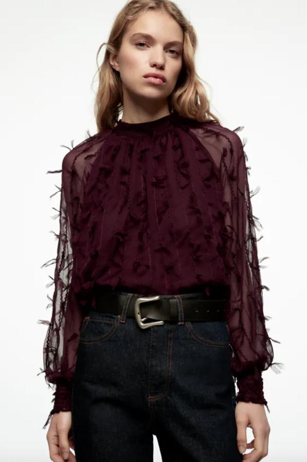 Cuello subido y mangas largas semitransparentes acabadas en puño elástico tipo nido de abeja para esta blusa de Zara en color granate con detalle de flecos en toda la prenda y forro interior a tono. Tiene un precio de 25,95 euros. 