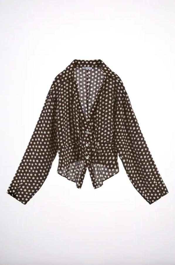 Tejido satinado en color marrón para esta blusa con estampado de lunares en blanco que podemos encontrar en Zara. Con cuello de solapa y escote de pico, tiene bajo asimétrico y cuesta 25,95 euros. 