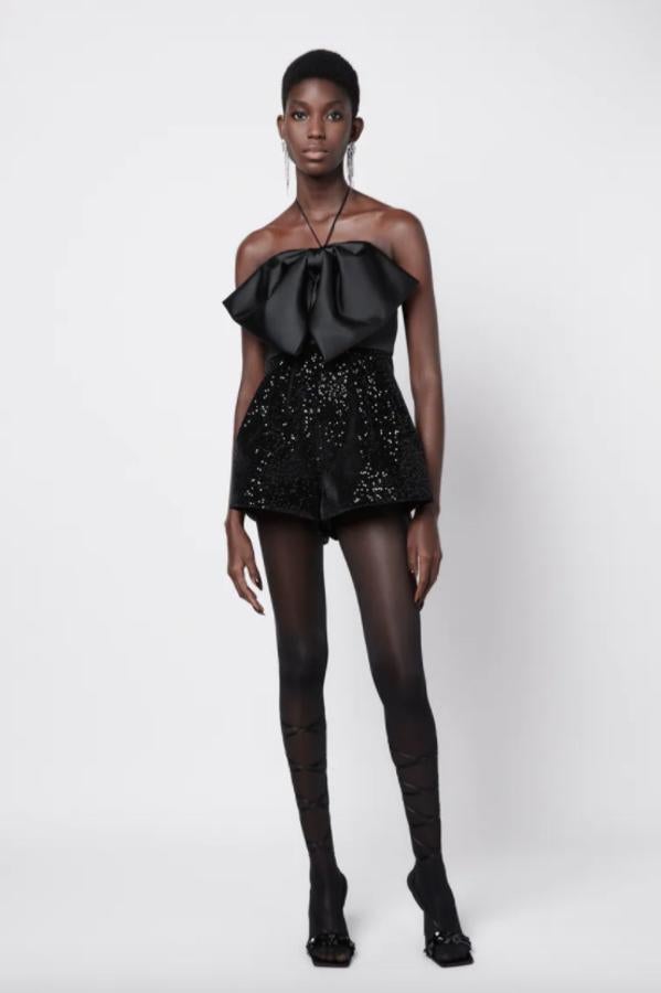 Con hombros descubiertos y tirantes dinos ajustables con lazadas, este mono corto de Zara con detalle de lazo con pliegues en la pechera y aplicación de lentejuelas en el cuerpo, tiene un precio de 59,95 euros. 