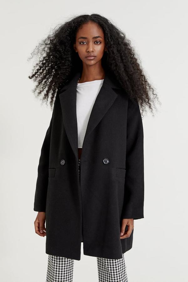 Diseño de hombros caídos para este abrigo negro de Pull&Bear que viene con cuello de solapa, cierre de botones a tono y bolsillos laterales al bies. Con puños acabados en falsos botones, cuesta 39,99 euros. 