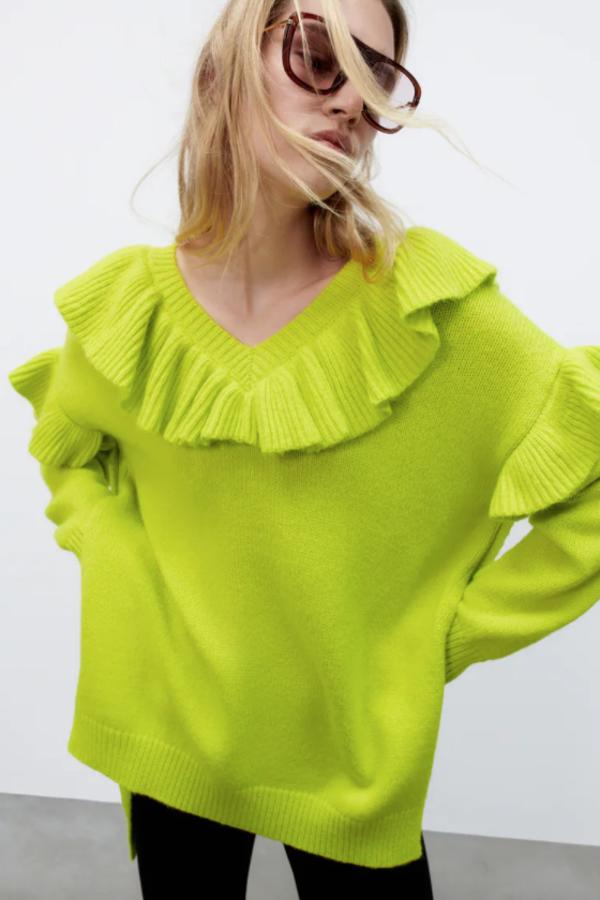 En color lima, con escote de pico y volantes en el cuello, hombros y mangas, este jersey de punto con bajo asimétrico, aberturas laterales y acabados en rib tiene un precio de 39,95 euros. 