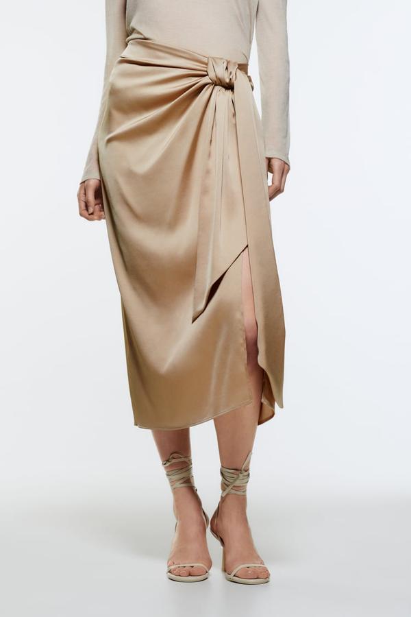 Con frunces y nudo, en color cava y con bajo con abertura frontal, esta falda midi con cremallera oculta en la espalda es de Zara, cuesta 25,95 euros y está disponible entre las tallas XS y XL. 