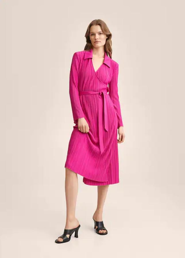 De diseño recto y en tejido plisado, este vestido de Mango con cierre cruzado de lazo lateral está disponible en fucsia, nego y marrón medio y tiene escote de pico con cuello de solapa y mangas largas. Está disponible entre las tallas S y XL y cuesta 29,99 euros. 