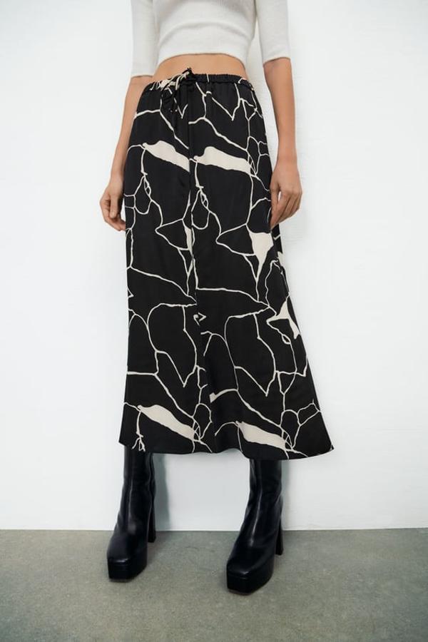 Esta original falda de Zara apuesta por los colores básicos para una prenda de diseño midi, tiro alto y con cintura elástica ajustable con cordones que tiene el bajo acabado en línea evasé y un precio de 29,95 euros. 