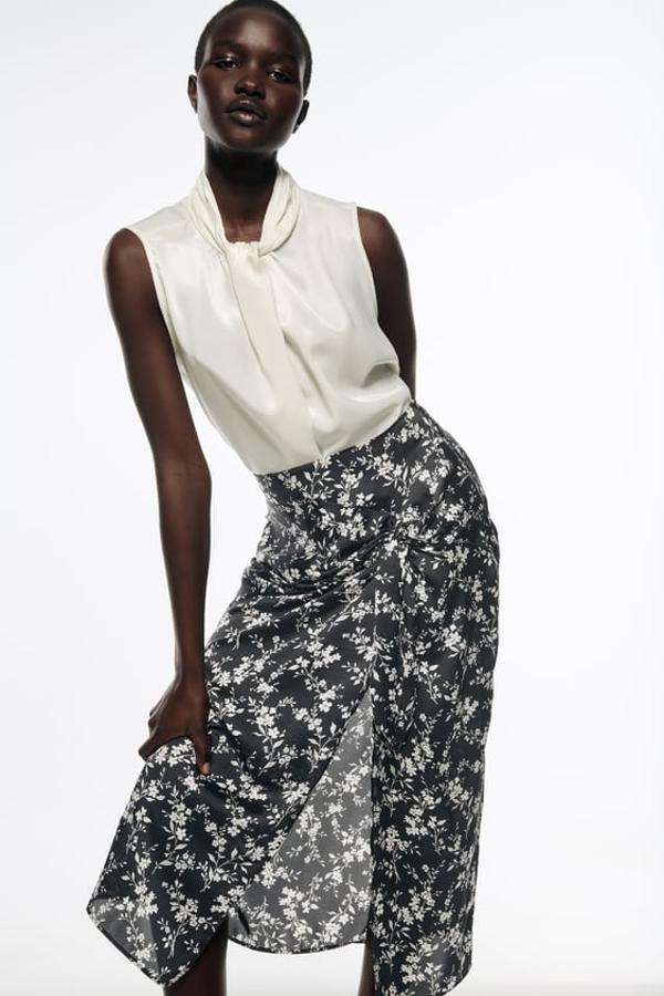 Estampado de flores blancas sobre fondo negro para esta falda midi de tiro alto con nudo delantero y bajo con abertura frontal que podemos encontrar en Zara por 25,95 euros. 