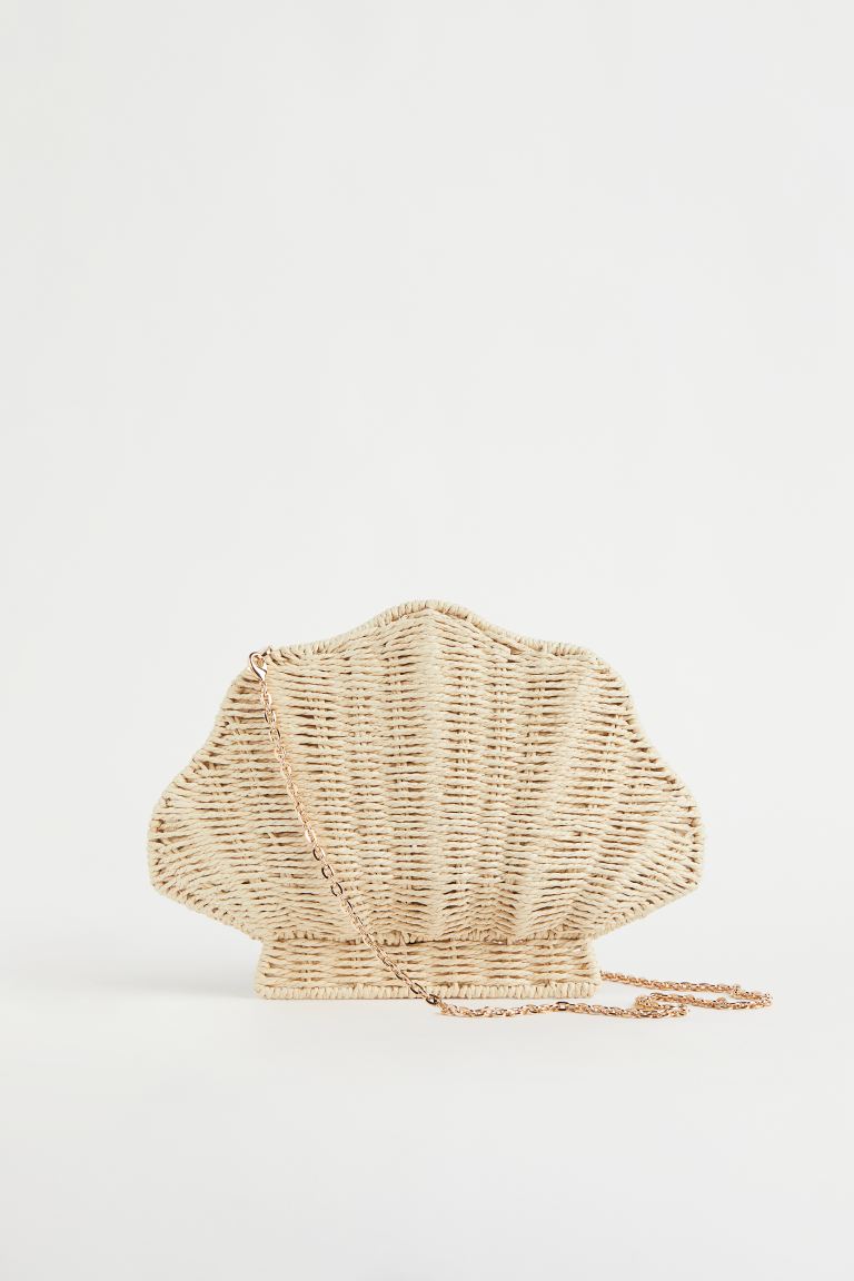 En beige claro, confeccionado en paja y con forma de concha, este bolso bandolera de H&M con correa extraíble de cadena de metal e interior forrado tiene un precio de 34,99 euros. 