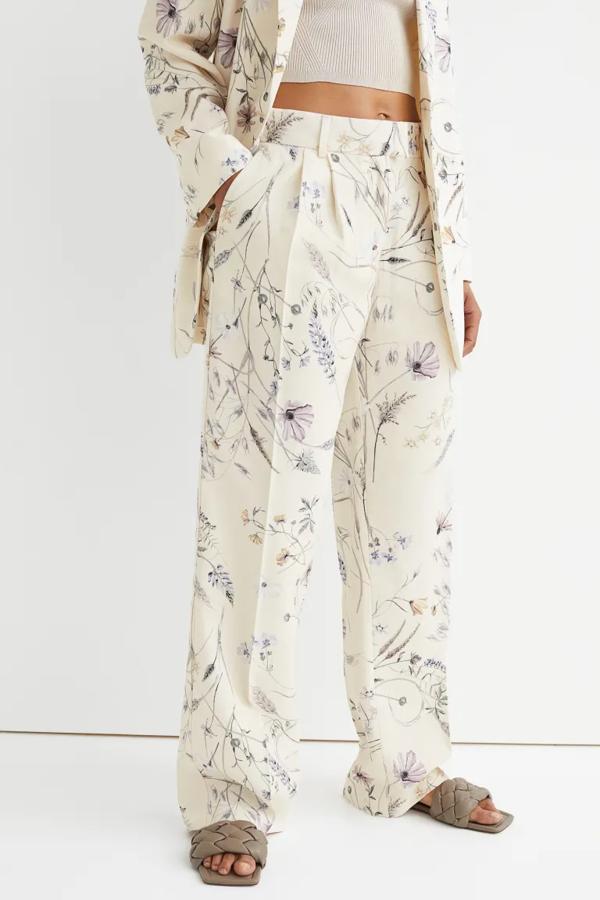 Fondo crema y estampado floral en lila para este pantalón de vestir en sarga de mezcla de viscosa que es de talle alto y tiene elástico revestido en la cintura. Con perneras amplias con raya, podemos comprarlos en H&M por 29,99 euros. 