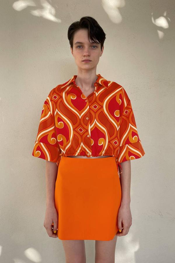 Camisa corta de Zara con manga amplia y estampado geométrico retro en naranja, rojo y blanco, con lazadas en el bajo ajustables, a 29,95 euros.