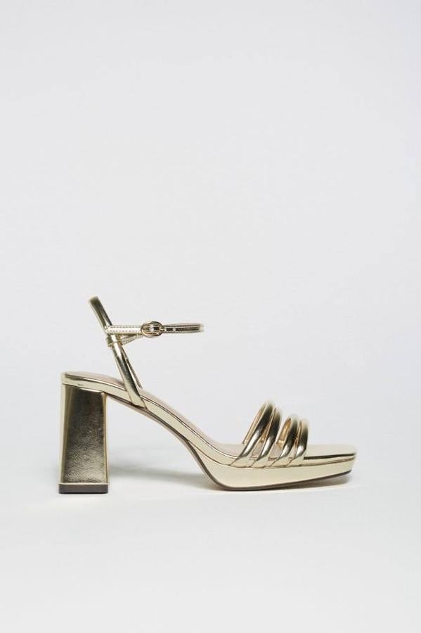 Zapatos de tacón ancho con plataforma, cierre de hebilla con pulsera al tobillo y tiras delanteras en tono dorado metalizad, de Sfera. Tienen un coste de 29,99 euros.