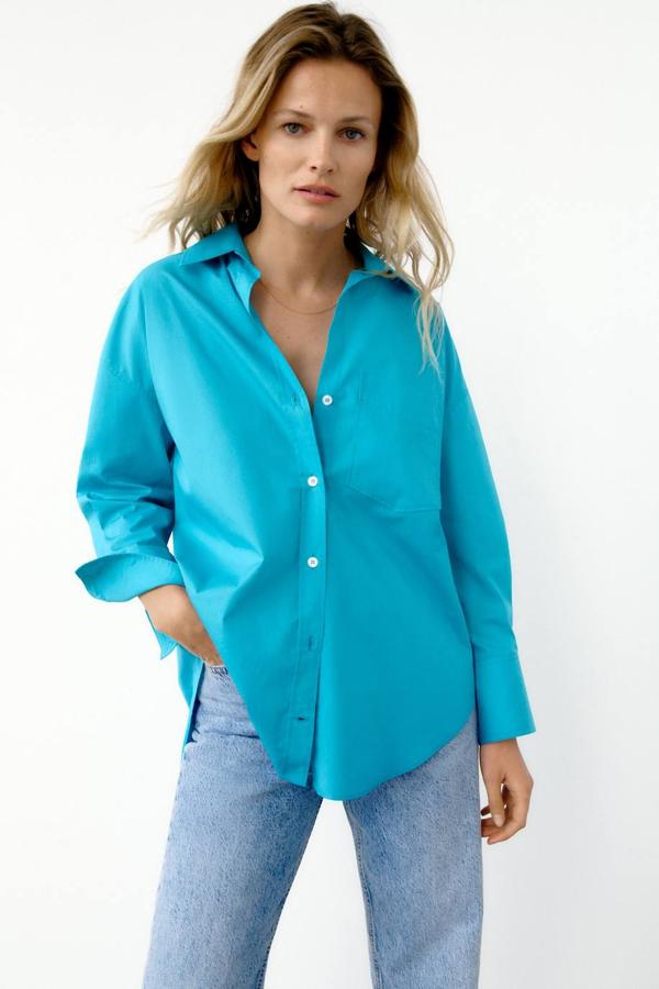 Camisa básica de popelín con manga larga, bajo asimétrico, cierre de botones delantero y bolsillo de plastrón, tono turquesa, de Zara. Su coste es de 19,95 euros.