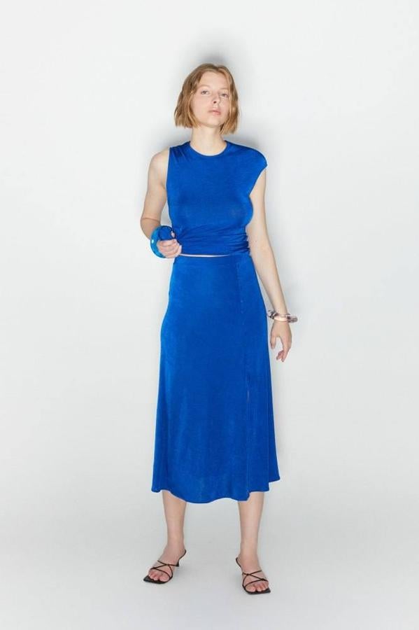 Falda midi confeccionada en tejido ligero y fluido con acabado brillante, talle alto y abertura lateral en el bajo con detalle de botones, color azul. Encuéntrala a 29,99 euros, en las tallas S, M y L.