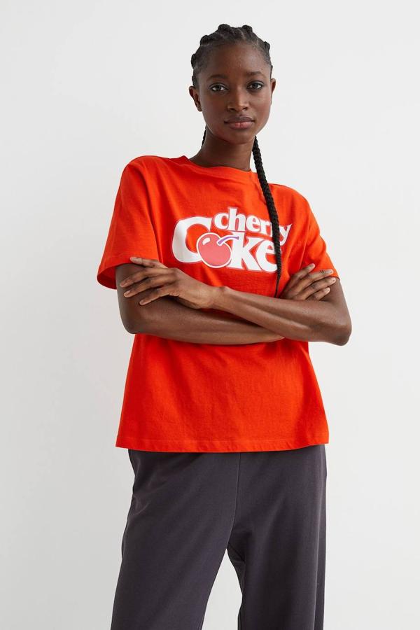 Camiseta de manga corta color rojo con motivo estampado ‘Cherry Coke’, de H&M. La encontrarás a 12,99 euros.