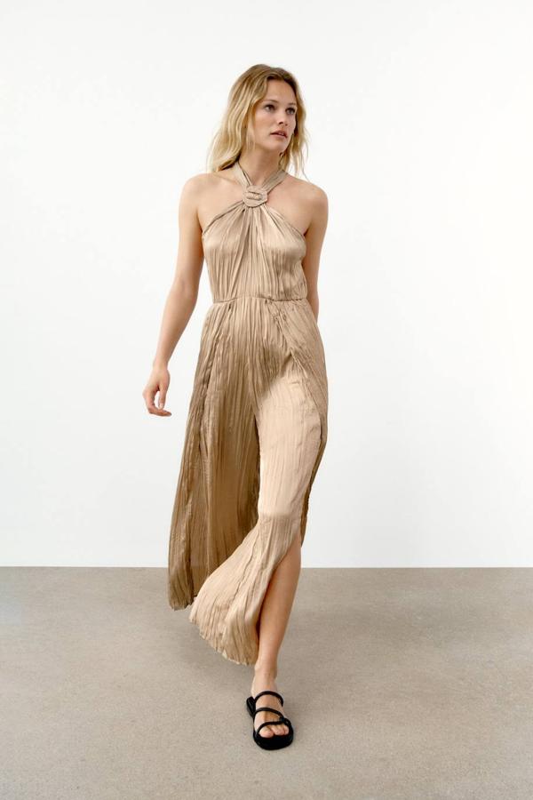 Mono de tejido satinado ligero efecto arrugado con cuello halter decorado con hebilla, cintura elástica y pernera ancha con aberturas, en tono piedra, de Zara. Su precio es de 35,95 euros.