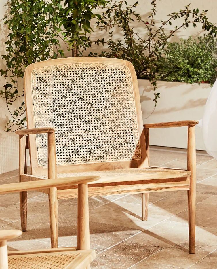 Las sobremesas al fresco serán mucho más agradables (y tu terraza o jardín quedarán mucho más bonitos) con esta butaca con reposa brazos de madera de teca y respaldo de ratán de Zara Home (249 euros).